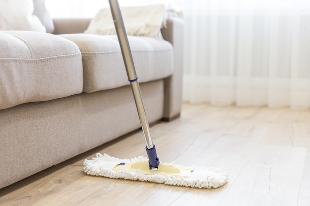 Cleaning floor with white mop near sofa