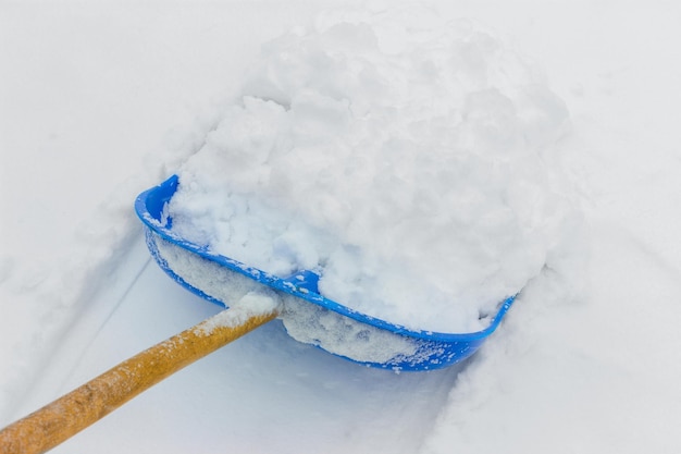 Cleaning fresh snow with blue plastic shovel outdoors in winter