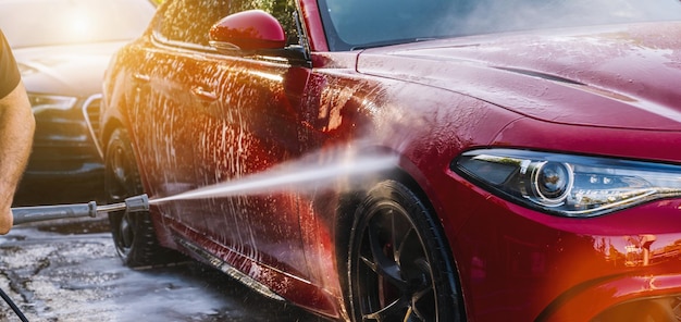 Cleaning red Car Using High Pressure Water in a Car Wash