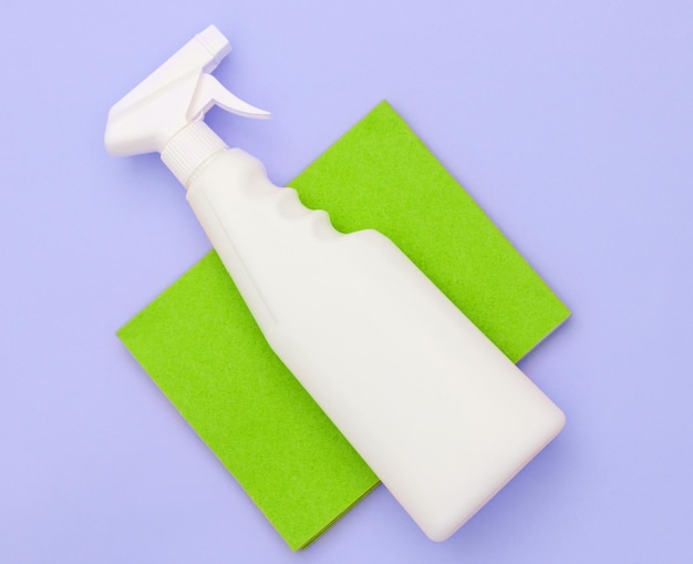 A cleaning spray lies on a green microfiber cloth. On a vjiolet background, top view.