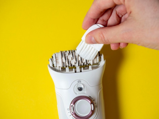 Cleaning a white epilator lying on a yellow background with a special brush Care for the device