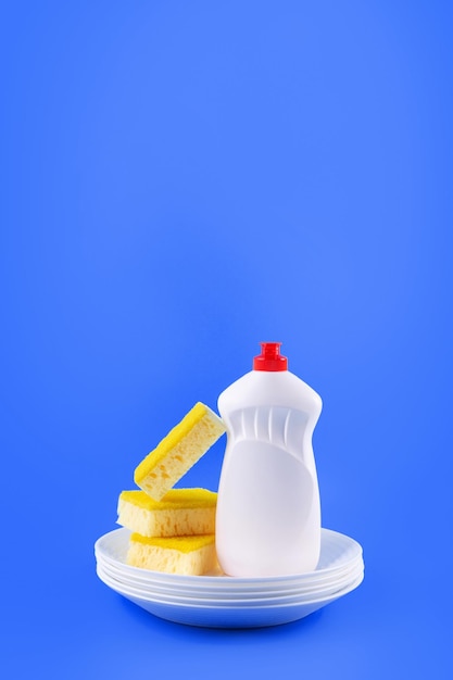 Cleaning yellow sponge white plate and detergent for dishes on a blue background Top view close up