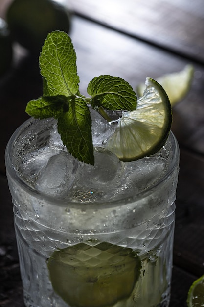 A clear carbonated drink in a glass glass with lime slices and fresh mint leaves