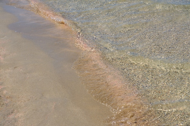 Clear waves and colorful sand on tropical sandy beach in Crete Greece.