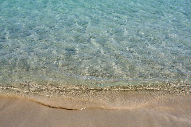 Clear waves and colorful sand on tropical sandy beach in Crete Greece.