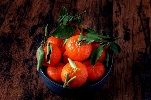 Clementines with leaves in a blue ceramic dish on an old wooden table