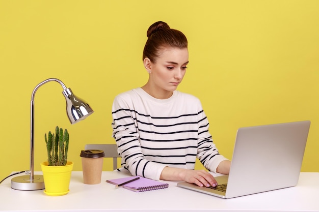 Clever businesswoman in striped shirt sitting on workplace seriously looking at laptop monitor