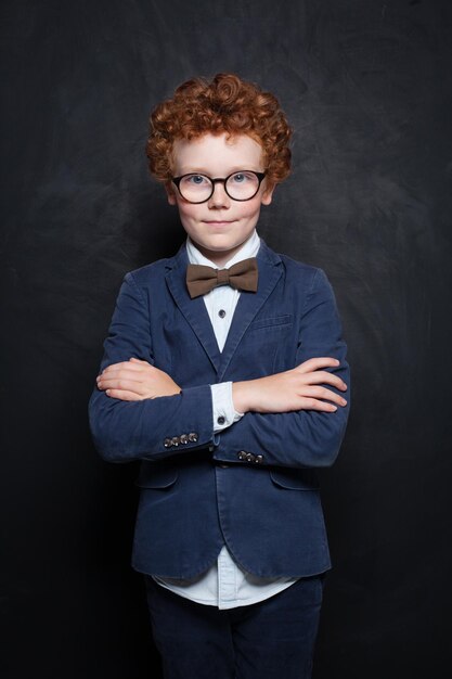 Clever child boy in glasses in classroom on chalkboard background Smart student portrait