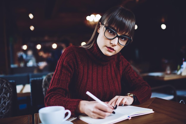 Photo clever female student spending time for autodidact sitting with textbook for education in cafeteria