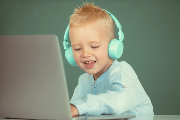 Clever school boy cute pupil wears headphones writing on laptop listen audio lesson use computer edu