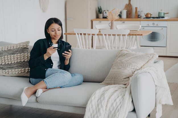 Client is purchasing online from home on quarantine Young woman holding smartphone and credit card