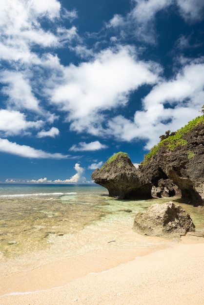 Cliffside beach, emerald green sea, blue sky, white clouds, coastal rocks. Iriomote Island.