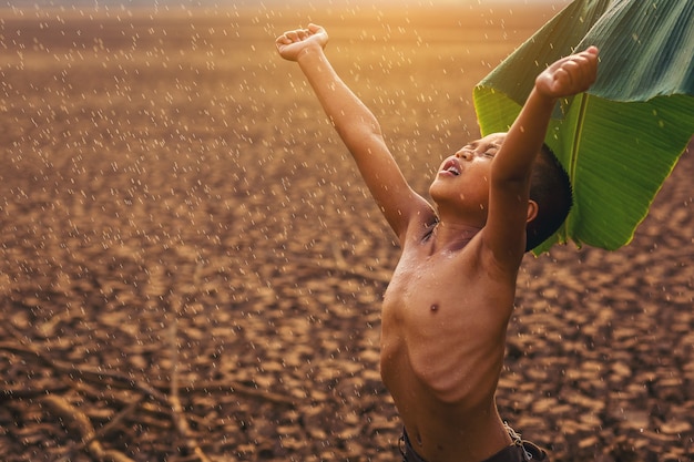 Climate change Asian boys enjoy with first falling rain season on dry cracked land Environment conservation and stop global warming concept