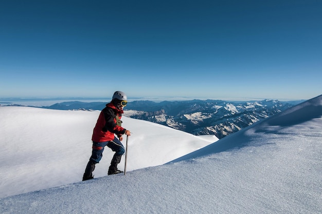 Climber in a red jacket climbs a mountain against a blue sky