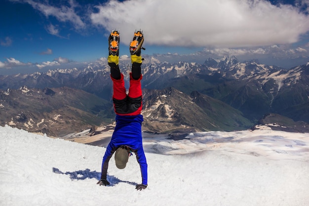 Climber standing upside down on his hands on top of the mountain