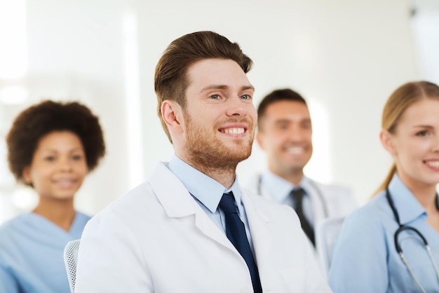 clinic, profession, people and medicine concept - happy male doctor over group of medics meeting at hospital