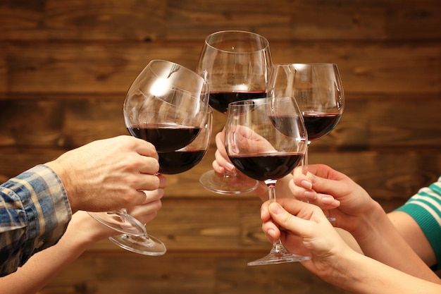 Clinking glasses of red wine in hands on rustic wooden planks background