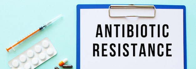 A clipboard with paper lies on a table near drugs and a syringe. Inscription ANTIBIOTIC RESISTANCE.