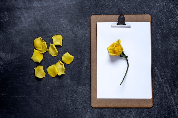 Clipboard with and a Petal of yellow rose on black background. Valentine's Day