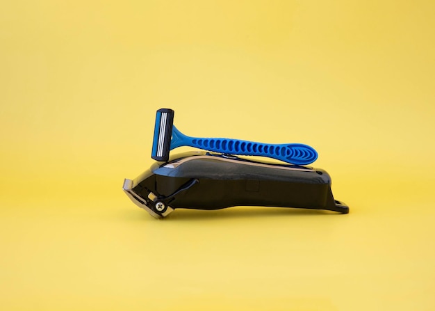 A clipper and a blue disposable razor lie on a yellow background