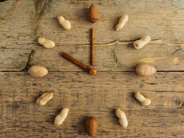 Clock made of different nuts and cinnamon on wooden table