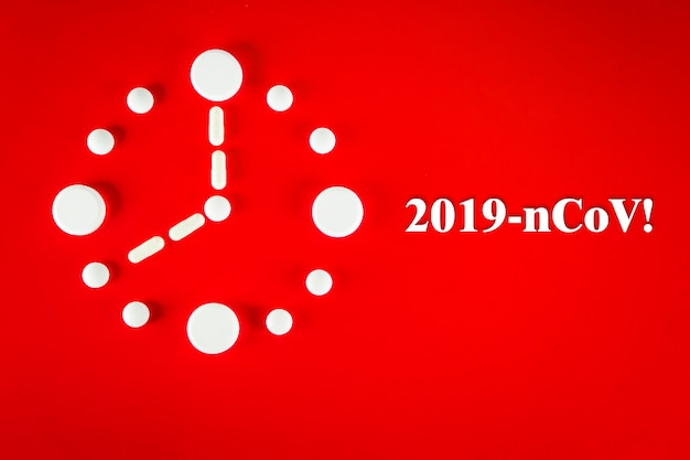 Clock made of white tablets with inscription 2019- nCoV , on red background, top view. 2019 Novel Coronavirus 2019-nCoV concept.