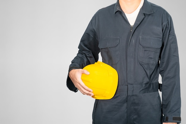 Cloes up Worker standing in blue coverall holding yellow hardhat isolated on gray background