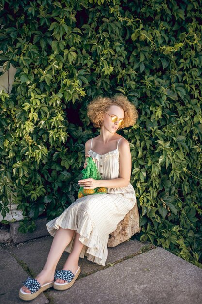 Close to nature. Pretty woman in a white long dress and sunglasses holding a green mesh bag in her hands