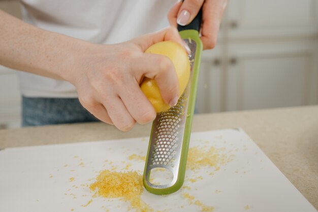 Photo a close photo of the hands of a woman rubbing zest of a lemon with a grater in the kitchen