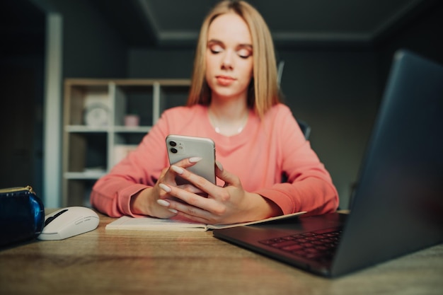 Close photo Lady uses the phone Female student sitting at desk at home with laptop