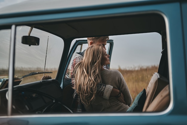 Close relationship... Beautiful young couple embracing while standing outdoors near the retro style mini van