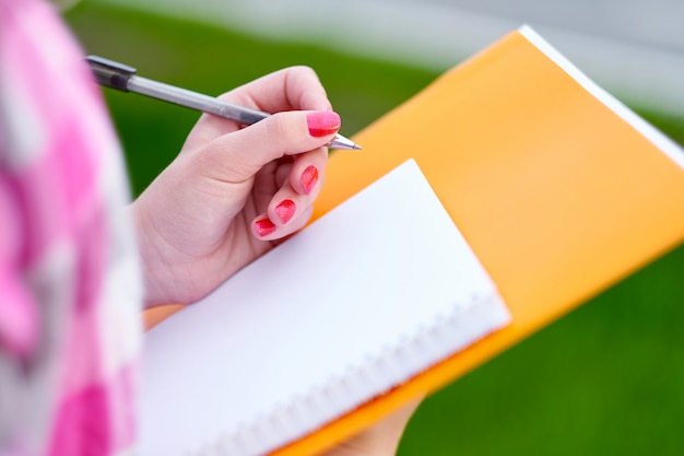 Close shot of student, woman hand writing something on the paper on the foreground. Opinion polls or statistics concept.