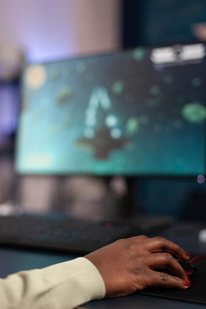 Close up of african american gamer holding hand on computer mouse playing space shooter video games during online championship. Pro player woman using RGB gaming equipment in home studio