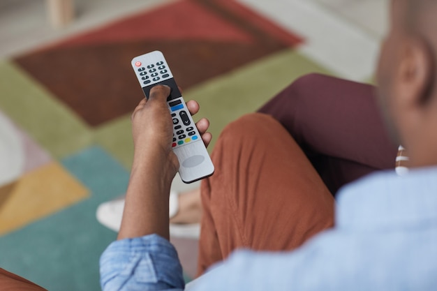 Close up of African-American man holding TV remote and switching channels, copy space