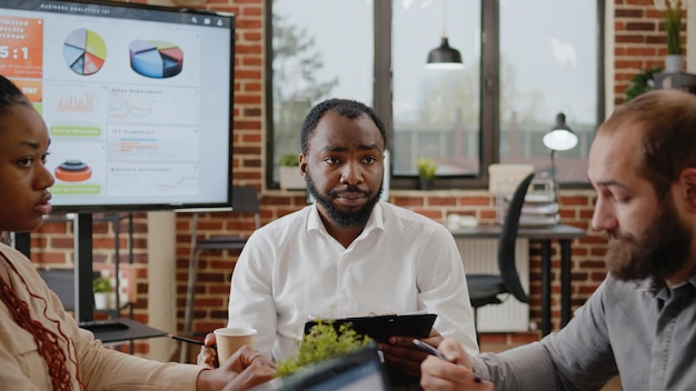 Close up of african american man talking about business project to workmates in boardroom office. Company worker presenting marketing strategy and analysis to group of people in office.