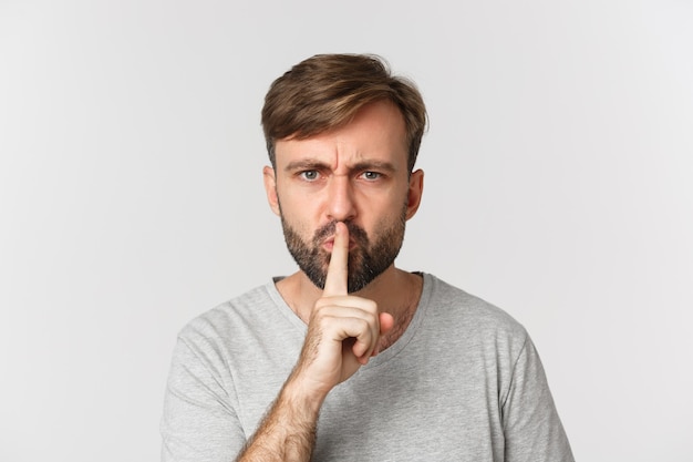 Close-up of angry caucasian man, shushing, telling to be quiet, frowning mad, standing over white.