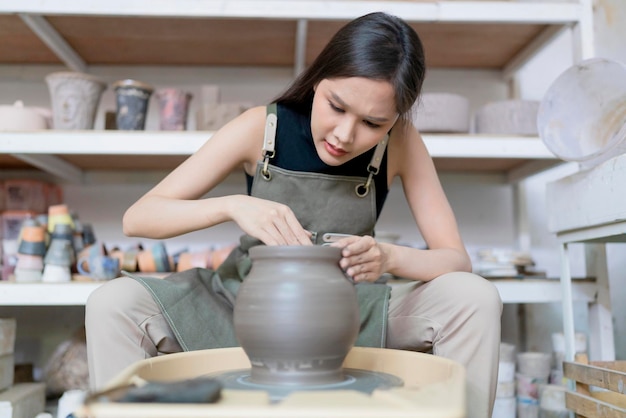 Close up of asian artist ceramist female hands working on potters wheelasian female sculpture woman with wet dirty hands shaping clay vase on pottery wheel at workshop studio