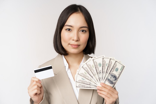 Close up of asian businesswoman office lady showing credit card and money dollars standing in suit over white background