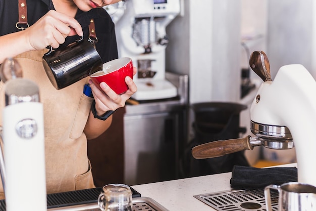 Close up of asian woman barista making cappuccino doing latte art in cup