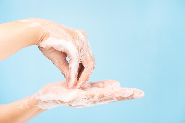 Close up of Asian women Cleaning hands with white soap bubbles on blue background. Hand washing demonstration for virus protection. Concepts of hygiene and prevention of covid 19