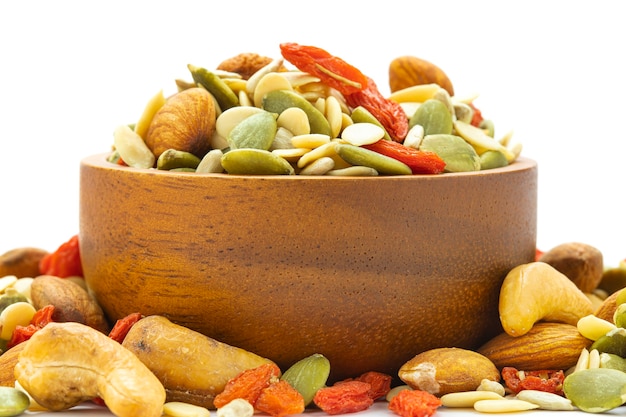 Close up assorted nuts are placed in a brown wooden cup on a white surface with almonds, sunflower seeds, melon seeds, cashews, seasoned kee.