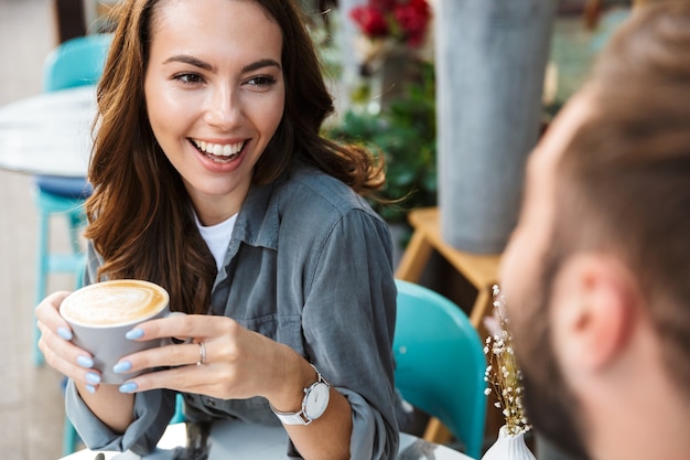 Close up of an attractive young couple in love having lunch while sitting at the cafe table outdoors, drinking coffee, talking