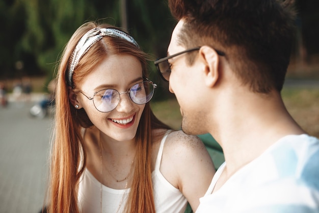 Close up of a attractive young red haired woman with freckles laughing with closed eyes while dating with her boyfriend outdoor in the park.