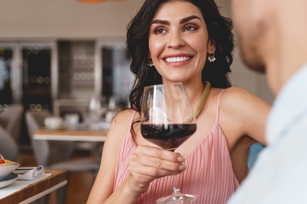 Close up of attractive young woman looking away and smiling while holding glass of wine