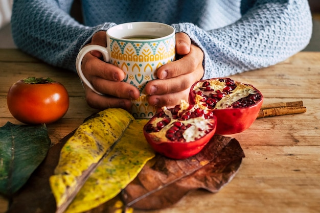 Close up of autumn home indoor scene with pair of hands hold a cup of tea on a wooden yellow and orange table with grapefruit and leaf