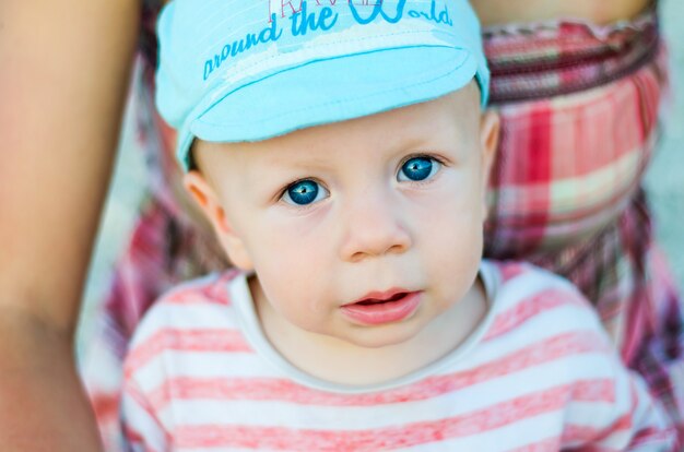 Photo close up of baby boy face with blue eyes with open mouth and blue cap. child and children emotions concept.