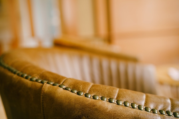 A close-up of the backrest of the chair, turning into an armrest made of brown genuine leather