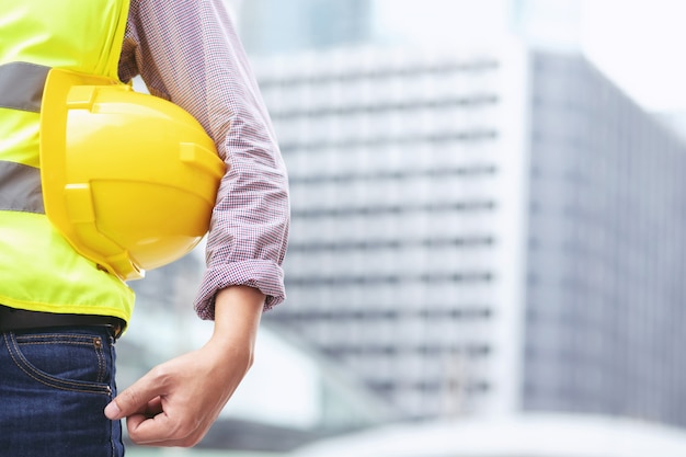 Close up backside view of engineering male construction worker stand holding safety yellow helmet and wear reflective clothing for the safety of the work operation.