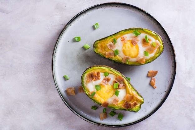 Close up of baked avocado with egg bacon and chives on a plate for a keto diet top view