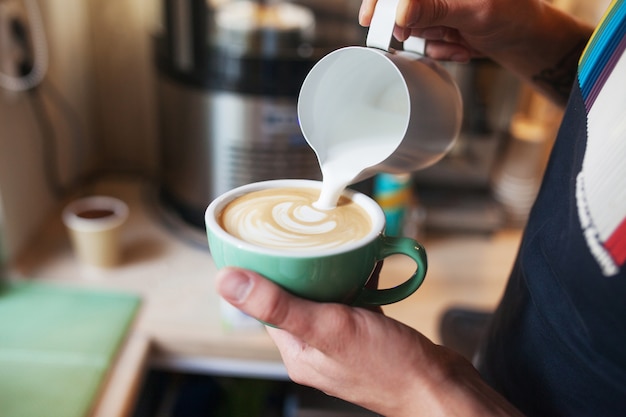 Close up barista hands pouring warm milk in coffee cup for making latte art.Professional coffee latte art in coffee shop.